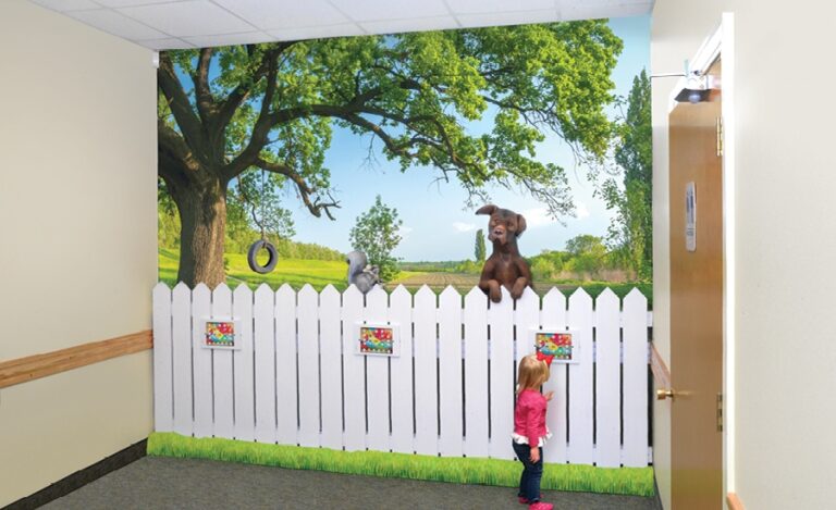 A gaming wall with 3 tablets on a white picket fence and a mural of a backyard with tree and tire swing.
