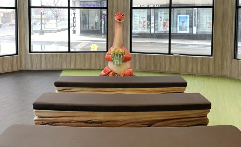 Custom bench row seats with sculpted dinosaur character holding a bag of popcorn in a kids theater area