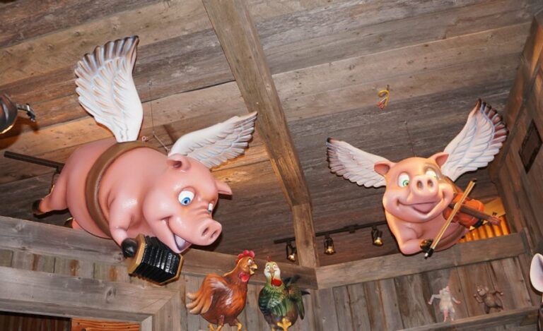 View of sculpted flying pig characters playing musical instruments suspended from the ceiling in a barnyard themed room.