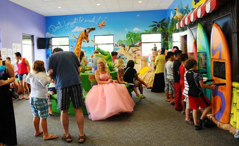 Kids in beach-themed pediatric waiting room with surfboard shaped gaming units, custom murals and 3D sculpted characters.