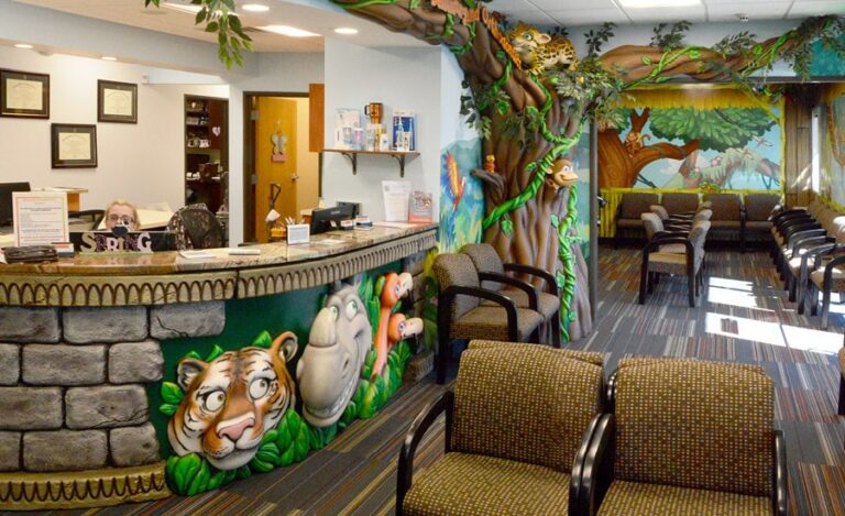 Jungle themed waiting area with wall murals and sculpted tree, vines and jungle characters. The reception desk has sculpted cladding of stone, tiger, rhino and flamingos.