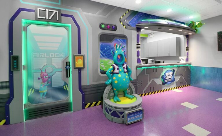 A space-themed reception area with wall murals and cladding made to look like the interior of a spaceship. A photo op sculpted alien greets visitors and a 3D sculpted alien and spaceship tops the reception desk.