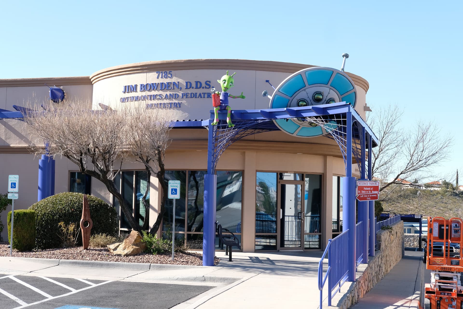A dental office building with the sign Jim Bowden, D.D.S. Orthodontics and Pediatric Dentistry features playful children's decor—a whimsical green alien figure at the entrance and a large smiling face above the awning, showcasing a cheerful transformation.