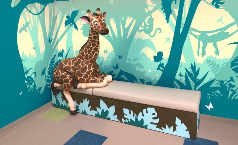 Friendly photo-op giraffe character perched on a cladded turquois, blue, and brown jungle theme bench set against contemporary silhouette wall mural in turquoise palette