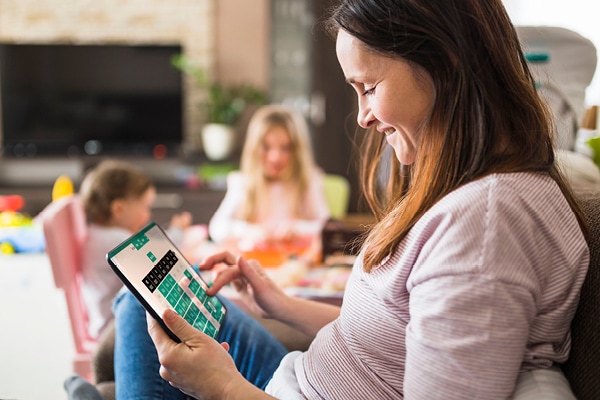 Mom playing a game on a tablet while her kids play in the background.