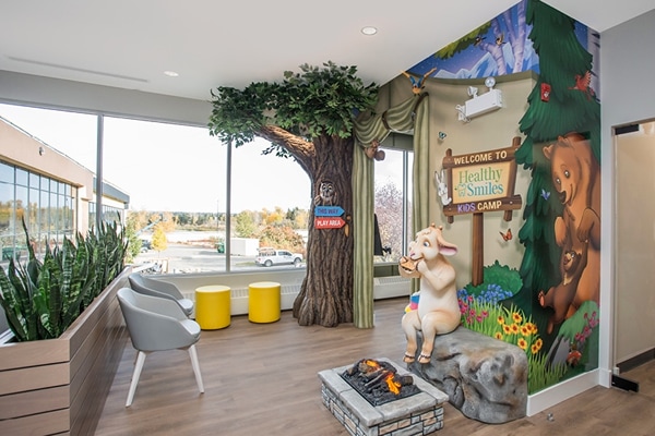 Forest themed kids corner in waiting room with a sculpted tree and a goat eating a s'more by the fire.