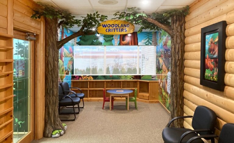 Woodland-themed entrance to a waiting room area decorated with 3D sculpted trees, 2D wall murals and faux window