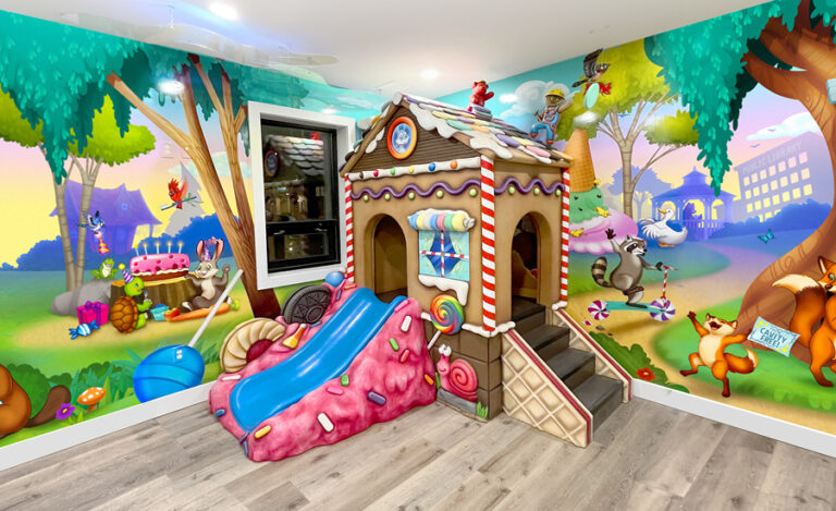 Candyland themed kid's play area with colorful wall murals and sculpted gingerbread house play structure with slide.