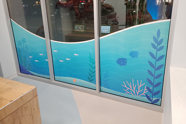 Decorative window panels with a colorful underwater scene show fish, seaweed, and coral against a blue background in a modern indoor setting.