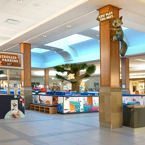 Family-friendly shopping mall play area with themed decor and central tree feature designed to attract children and families