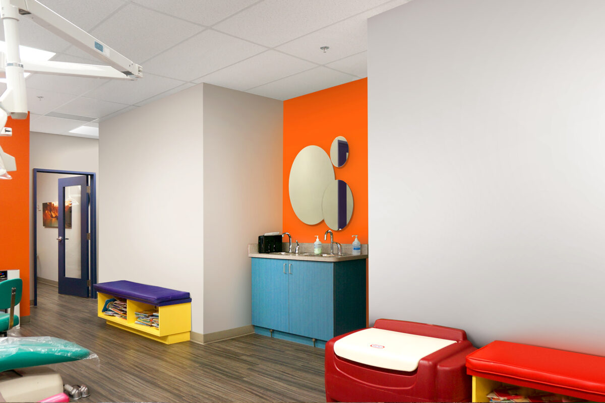 A brightly colored pediatric waiting room—far from drab—with orange and gray walls, a blue cabinet and playful oval mirrors, plus colorful benches with storage and a red padded bench on wood-patterned flooring.