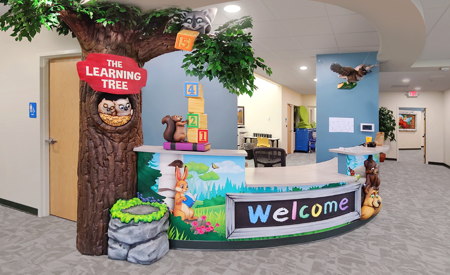 Woodland themed reception desk with sculpted owls in a tree, mossy rock, animal characters and wall murals.
