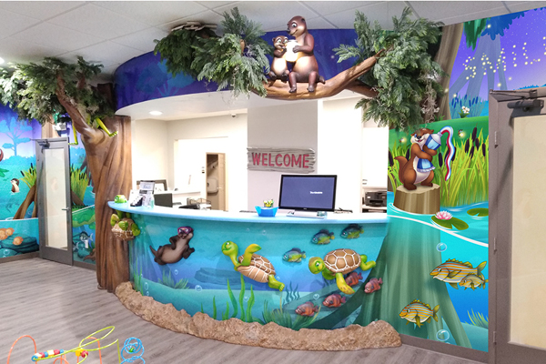 Colorful pediatric reception desk decorated with jungle and underwater animal murals, featuring turtles, otters, and fish. Stuffed animals and greenery create a playful atmosphere that often earns rave IDS testimonial reviews from delighted families.