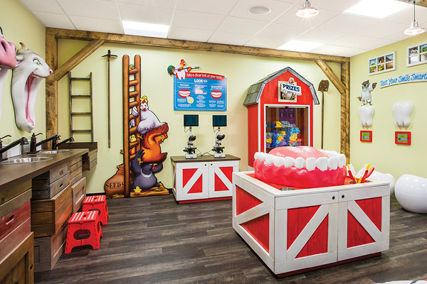 A colorful, farm-themed children’s play area features animal murals, a giant model of teeth, prize barn, red stools, sinks, and games, creating a fun and friendly dental office environment.
