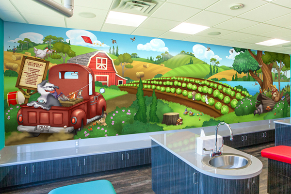 Colorful mural of a farm scene with a red truck, barn, green fields, and playful animals. The mural decorates a modern room with sinks and blue and red stools in the foreground.