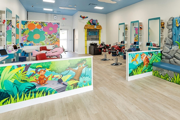 Colorful childrens hair salon with playful wall murals, toy car salon chairs, and cartoon animal decorations. Bright, cheerful space with a blue ceiling, mirrors, and a fun, welcoming atmosphere for kids.