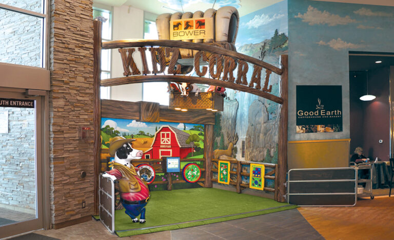 This image shows the entrance to a farm-themed play area in a rodeo-themed mall. The entrance features a rustic wooden sign that reads