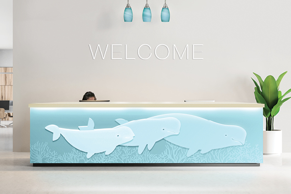 A Pediatric Front Desk features three blue beluga whales illustrated on the front, “WELCOME” above, blue pendant lights overhead, and a large green plant to the right, creating a cheerful and inviting atmosphere for young visitors.