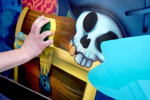A hand holding a sponge cleans an easy to clean IDS mural.