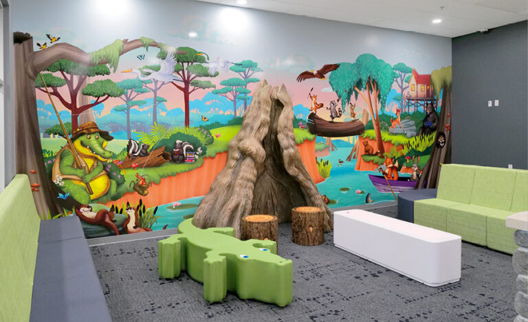 A colorful, bayou-themed pediatric medical health center waiting room with a wall mural of animals by a river, a tree stump play structure, green benches, log stools, cushioned seating, playful decor, and a soft carpeted floor.